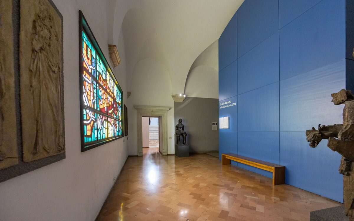 Sala museale scura con grandi schermi video e postazioni di pietra dell’installazione di Studio Azzurro.