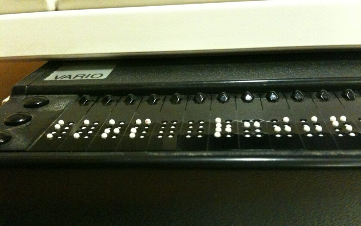 Una mano tocca le celle di un display Braille aggiornabile accanto a una tastiera.