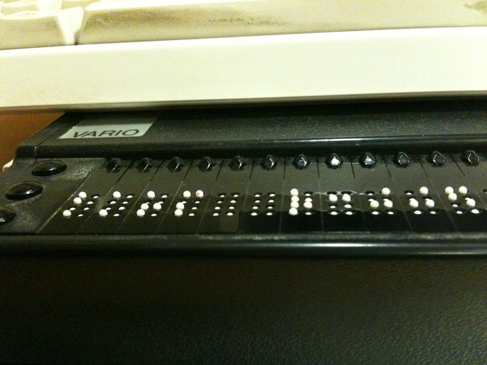 Una mano tocca le celle di un display Braille aggiornabile accanto a una tastiera.