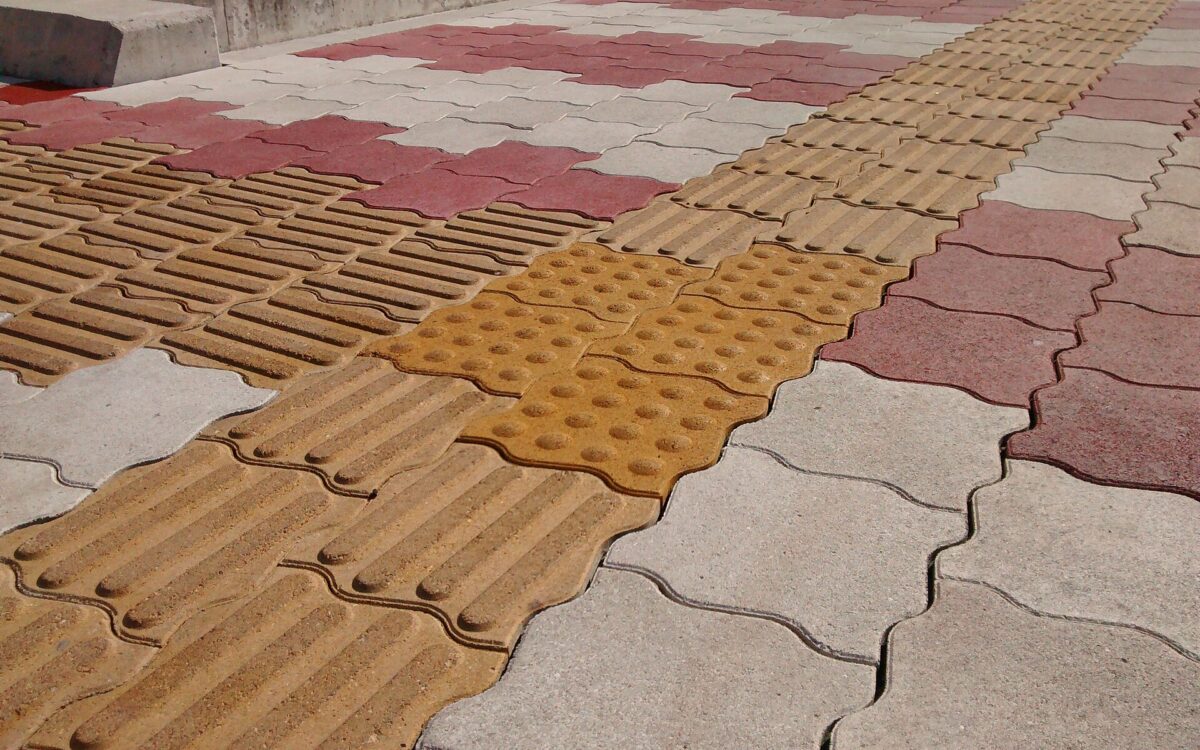 Fascia di mattonelle tattili gialle con rilievi lineari attraversa una pavimentazione urbana in Giappone.