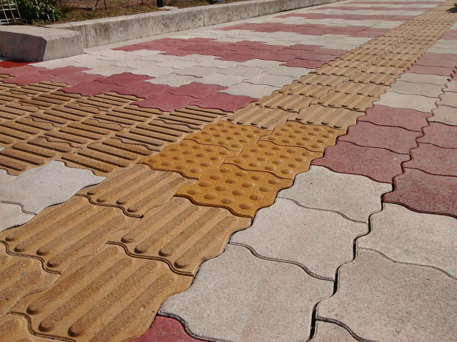 Fascia di mattonelle tattili gialle con rilievi lineari attraversa una pavimentazione urbana in Giappone.
