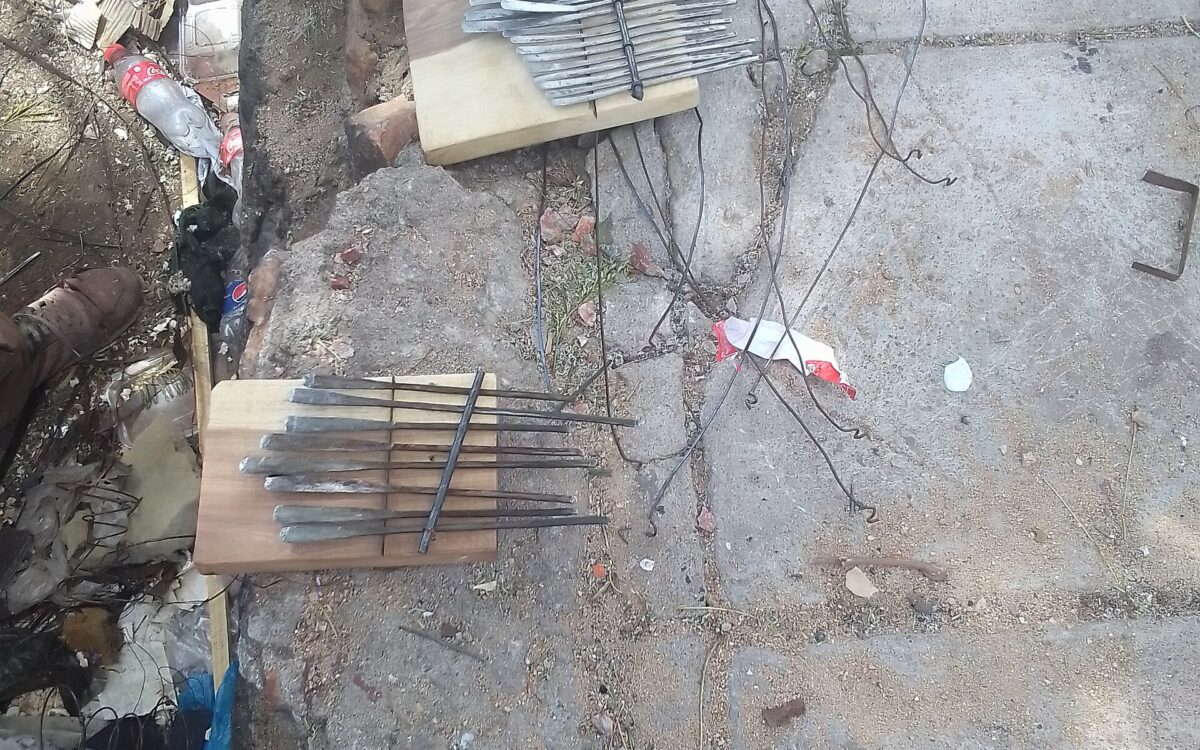 Mani sistemano lamelle metalliche parallele su una tavola di legno durante la costruzione di una mbira.
