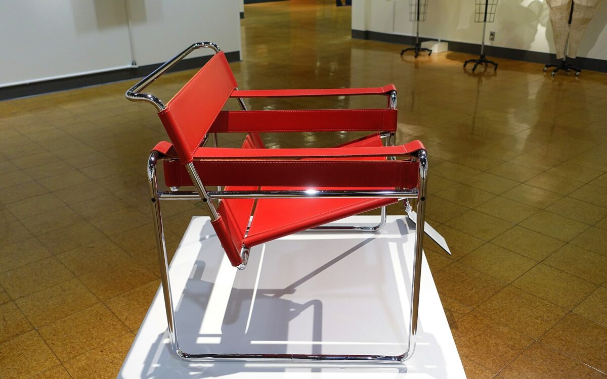 Una Wassily Chair in tubolare d’acciaio cromato e fasce scure, fotografata di tre quarti in uno spazio museale.
