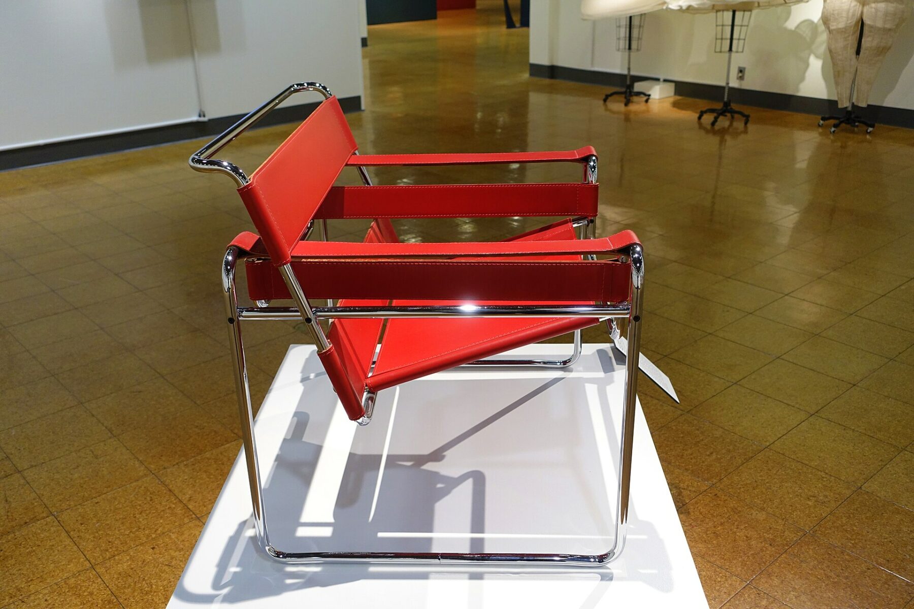 Una Wassily Chair in tubolare d’acciaio cromato e fasce scure, fotografata di tre quarti in uno spazio museale.