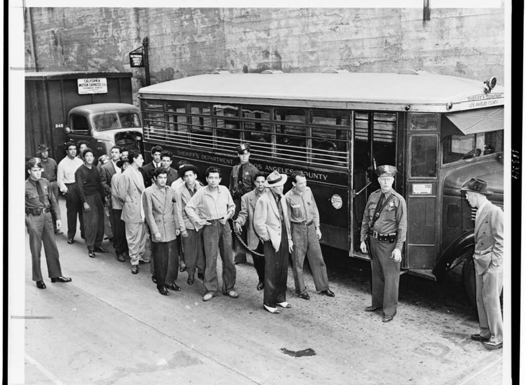 Fotografia in bianco e nero di giovani in completi zoot in fila davanti a un edificio a Los Angeles nel 1943.
