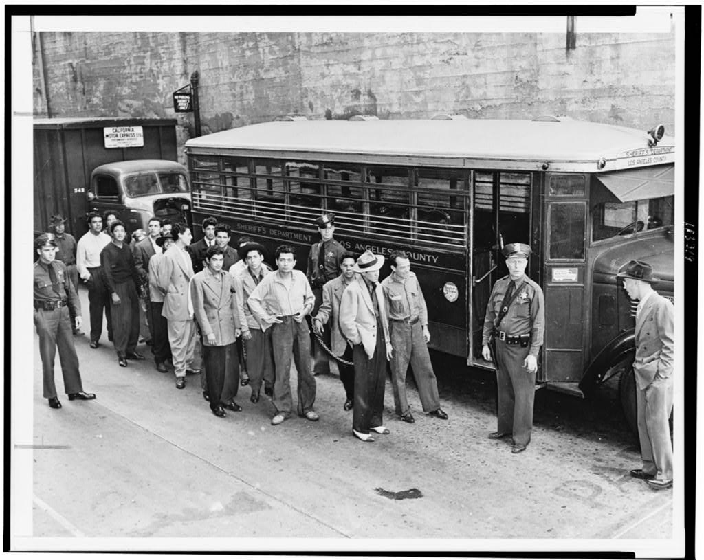 Fotografia in bianco e nero di giovani in completi zoot in fila davanti a un edificio a Los Angeles nel 1943.