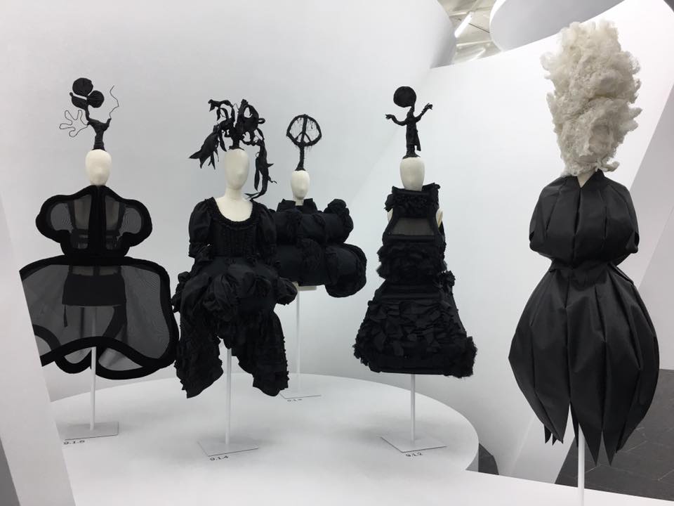 Manichini con abiti scultorei di Rei Kawakubo esposti in un ambiente museale bianco.
