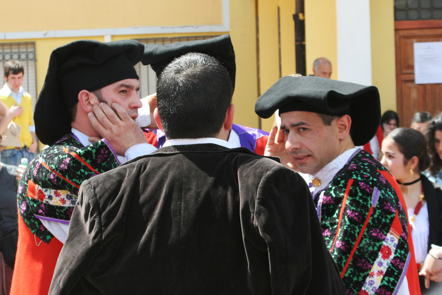 Quattro uomini in abiti tradizionali cantano molto vicini formando un piccolo cerchio durante un evento pubblico in Sardegna.