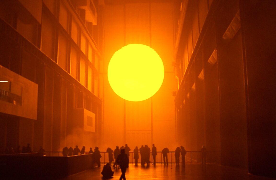 Il grande sole artificiale di The Weather Project illumina la Turbine Hall della Tate Modern, con visitatori distesi e riuniti sul pavimento.