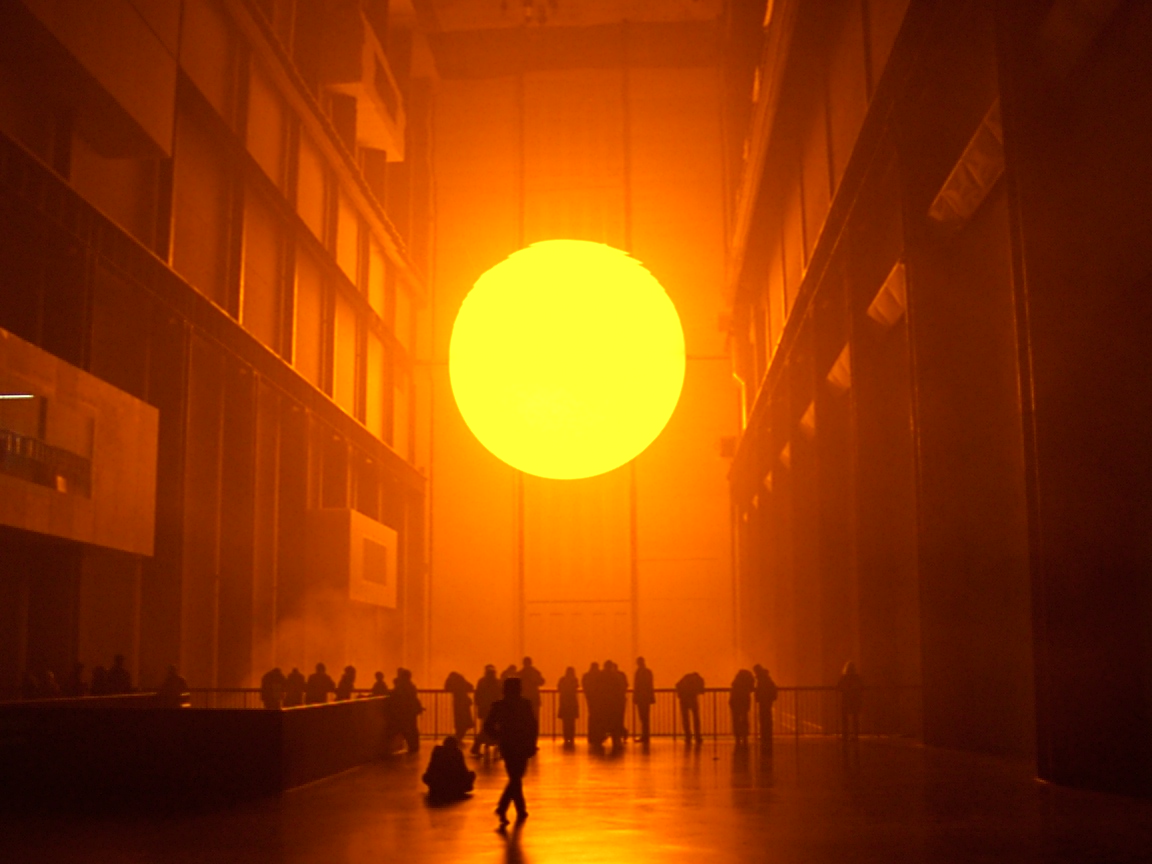 Il grande sole artificiale di The Weather Project illumina la Turbine Hall della Tate Modern, con visitatori distesi e riuniti sul pavimento.